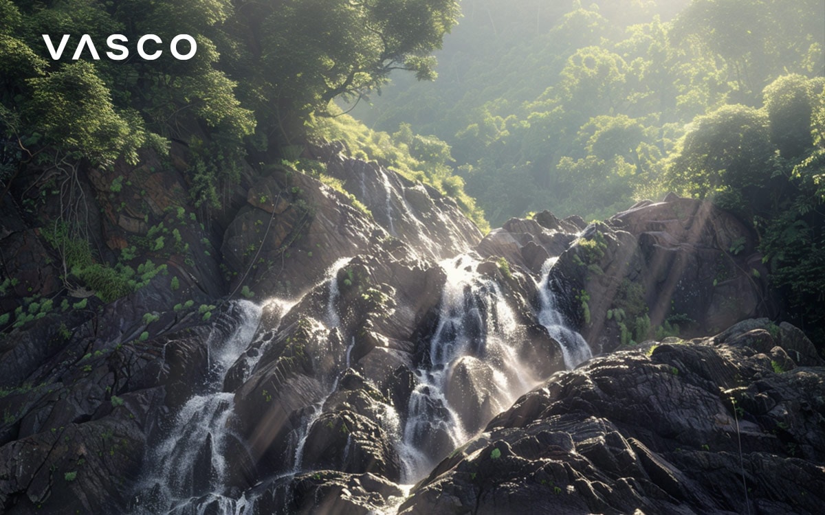 A cascading waterfall surrounded by lush green forest in sunlight