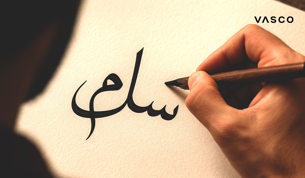 Ruka píše arabskú kaligrafiu štetcom na papier