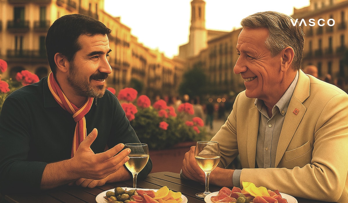 Dvaja muži si vychutnávajú drinky a tapas vo vonkajšej kaviarni na Španielskom námestí a rozprávajú sa s kvetmi a architektúrou v pozadí.