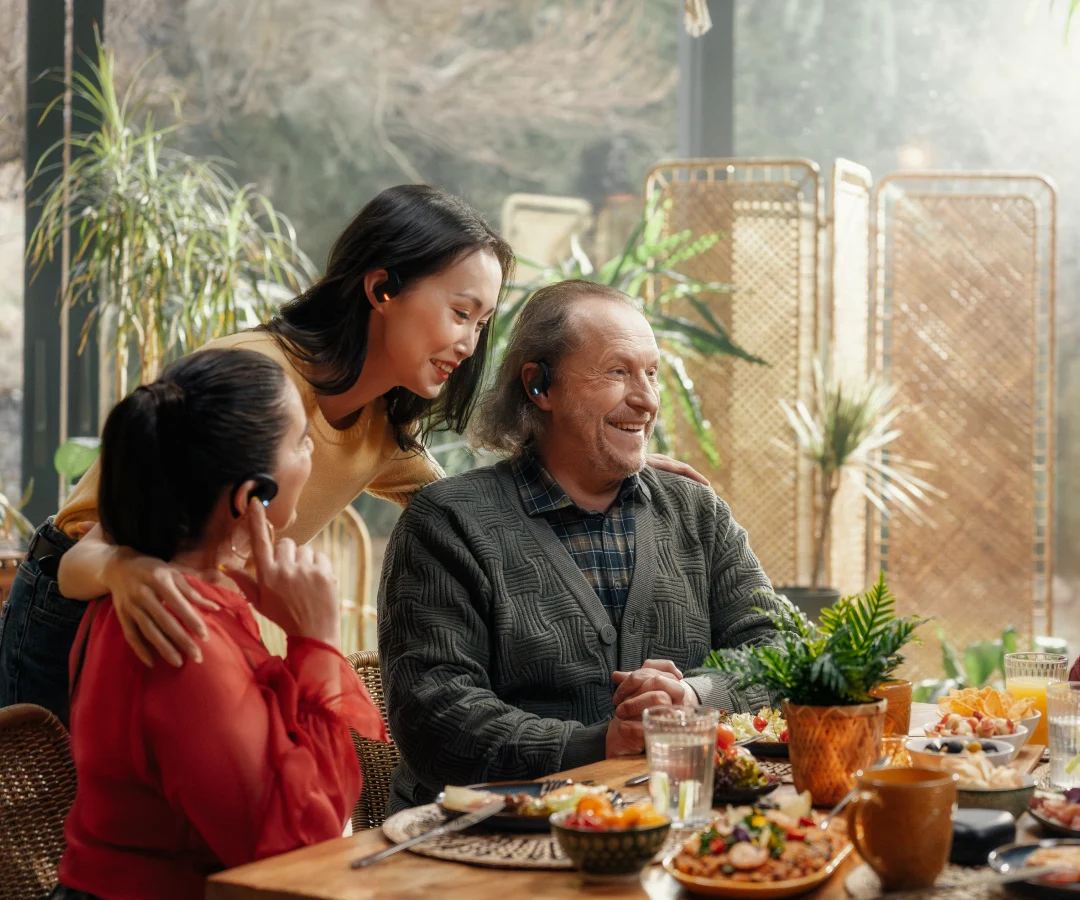 a group of smiling people sitting at a table during family meeting with translating headphones on their ears