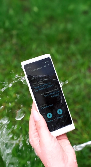 Detail ruky držiacej Vasco Translator V4, na ktorý strieka voda, čím sa zdôrazňuje jeho odolnosť.