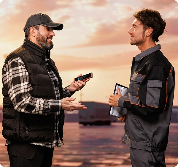 Dvaja muži spolu komunikujú; vodič kamióna drží Vasco Translator V4 a pracovník skladu oproti nemu má v rukách dokumenty. Komunikujú pomocou zariadenia Vasco.