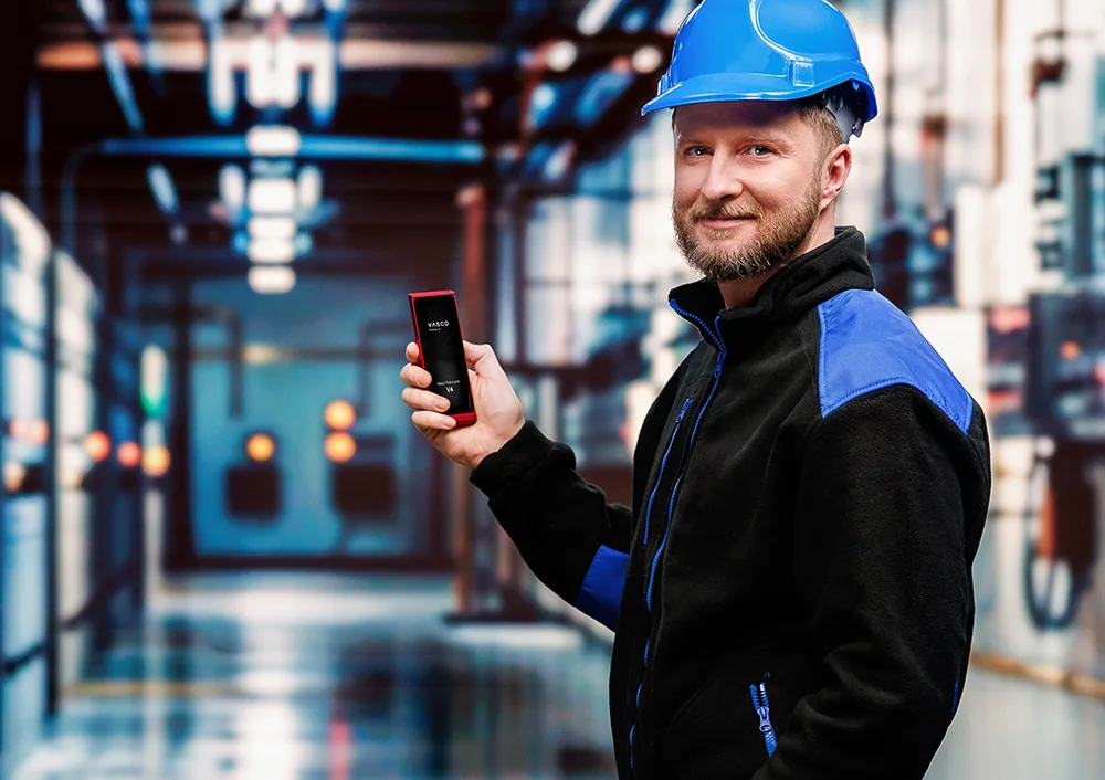 Vodič kamióna stojí pred vozidlom, v jednej ruke drží dokumenty a v druhej Vasco Translator V4, pričom na displeji je zobrazená funkcia prekladu z fotografie.