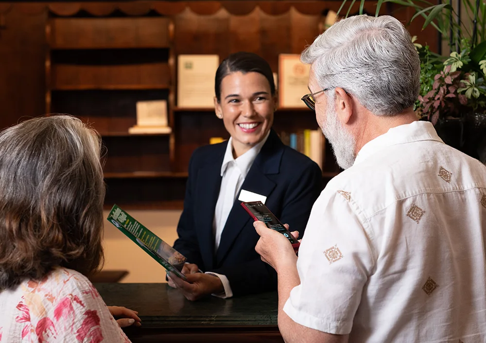 Usmiata recepčná počúva preklad z Vasco Translator V4, ktorý k nej smeruje muž držiaci zariadenie.