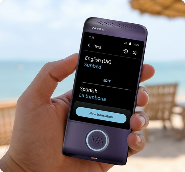 Záber zblízka na ruku, ktorá drží fialové elektronické prekladateľské zariadenie značky Vasco. Na obrazovke je zobrazený preklad textu z angličtiny (britská) do španielčiny, kde je slovo „Sunbed“ preložené ako „La tumbona“. Pozadie tvorí jasná, slnečná plážová scéna s rozmazaným výhľadom na more, zlatistý piesok, niekoľko ležadiel a slamený plážový dáždnik. 